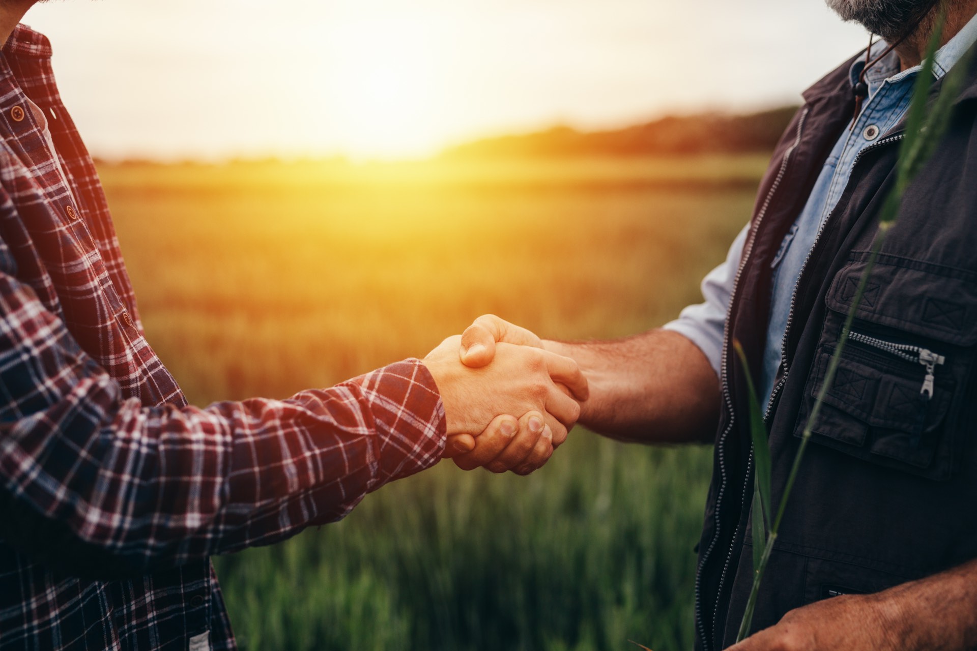 Two farmers shaking hands in a Kansas field at sunset